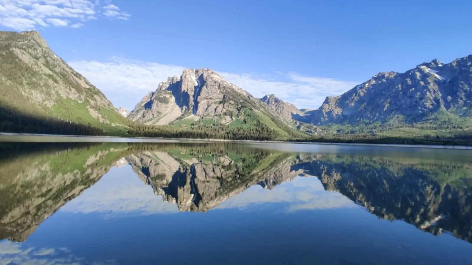 Calm lake with mirror-like reflection and multiple mountain peaks with rocky faces in Yellowstone National Park.